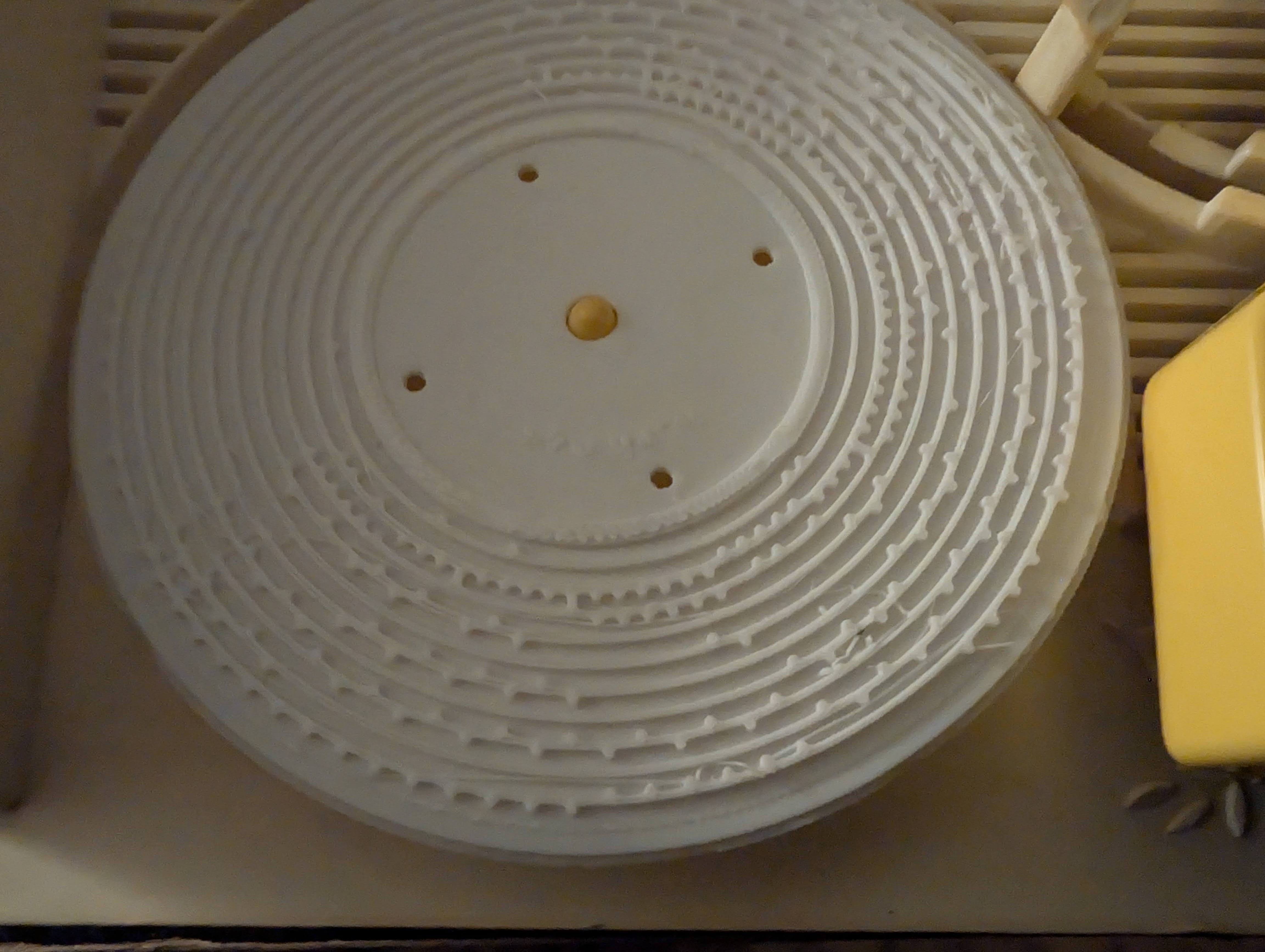 The first 3D-printed disc sitting on the Fisher Price record player, showing concentric rings of raised note bumps in white PLA